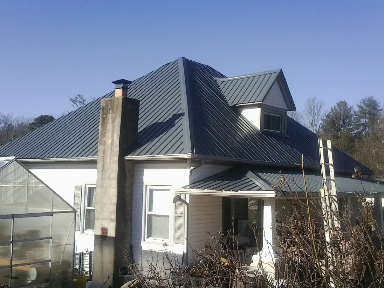 Dark blue standing seam metal roof on a white farmhouse with dormer — Slate & Tile Roof Repair by Roofing Brothers in Marshall