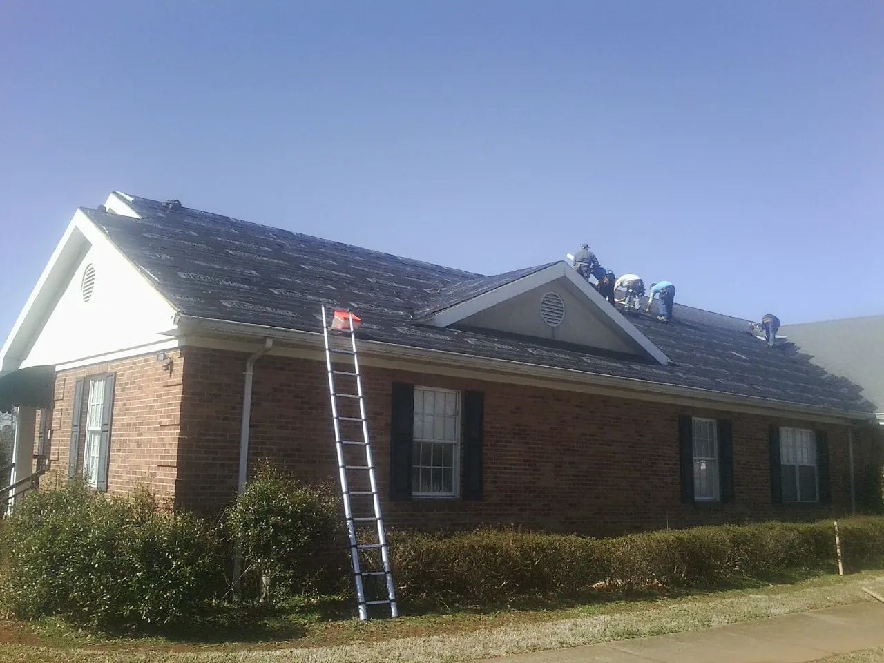 Crew tearing shingles off a brick ranch roof with a ladder set — Emergency Roof Repair work by our crew in Marshall